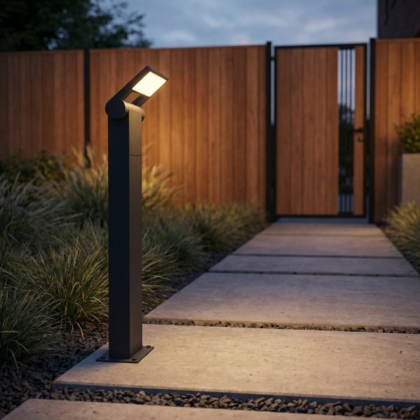 Moderne LED-Außenstehleuchte beleuchtet einen Gartenweg aus Betonplatten, Holzzaun und Ziergräser im Hintergrund in der Abenddämmerung.