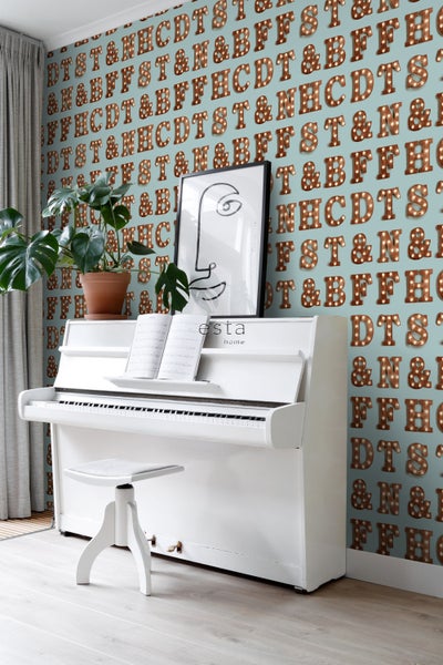 Szene mit weißem Klavier, Hocker, Zimmerpflanze und Tapete mit Buchstabenmotiven