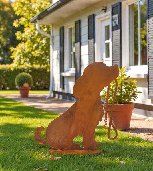 Gartenstecker in Form eines Hundes aus Edelrost auf einer Rasenfläche vor einem Wohnhaus.