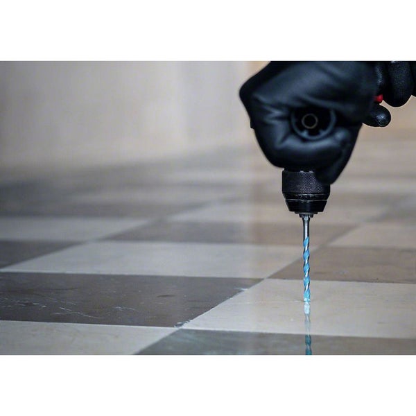 Eine Person bohrt mit einer Bohrmaschine und einem Bohrer in einen gefliesten Boden.