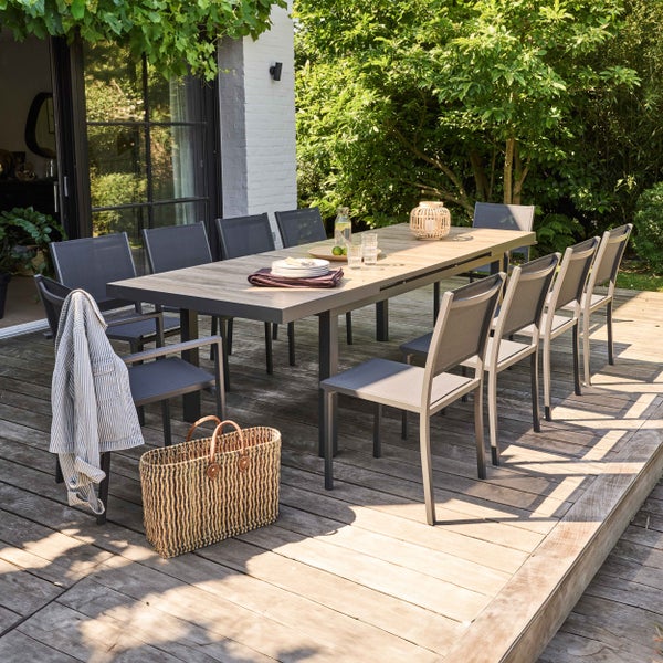 Modernes Gartenset mit großem rechteckigem Esstisch in Holzoptik und zehn passenden Stühlen auf einer hellen Holzterrasse im Garten.