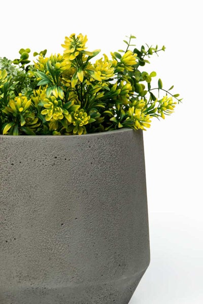 Kunstpflanze mit gelben Blüten in einem grauen Pflanztopf in Betonoptik.