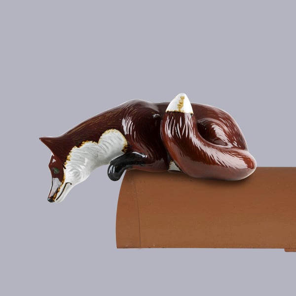 Dachschmuck Firstfigur Fuchs aus glasierter Keramik, liegend auf einem Firstziegel.