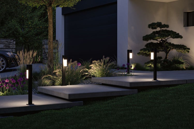 Moderne schwarze Wegeleuchten beleuchten einen Gartenpfad aus Betonstufen in der Dämmerung, umgeben von Ziergräsern und Blumen.