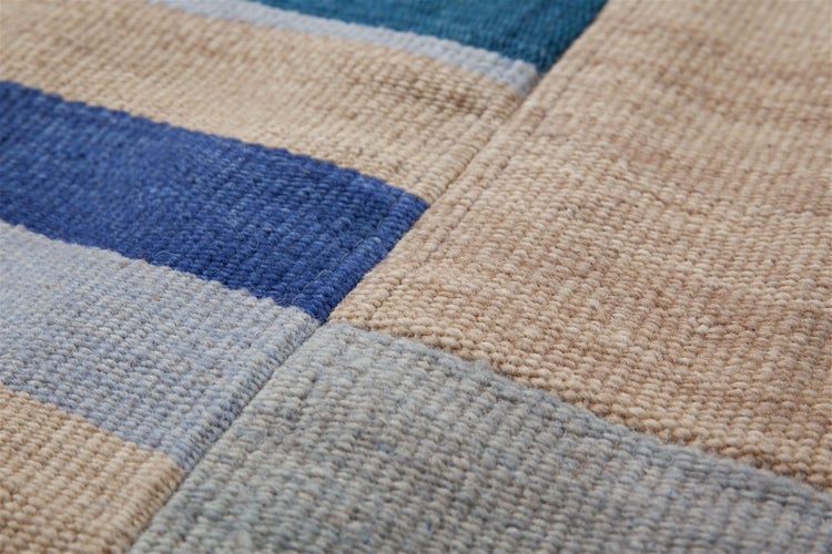 Nahaufnahme eines gewebten Teppichs mit geometrischem Blockmuster in Blau, Beige und Grau sowie sichtbarer Textilstruktur.