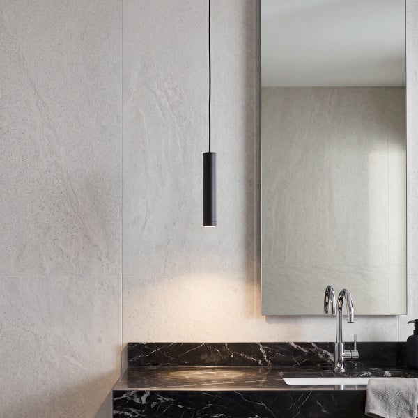 Modernes Badezimmer mit Waschtisch aus dunklem Marmor, Wandspiegel, Pendelleuchte und hellen Steinfliesen an der Wand.