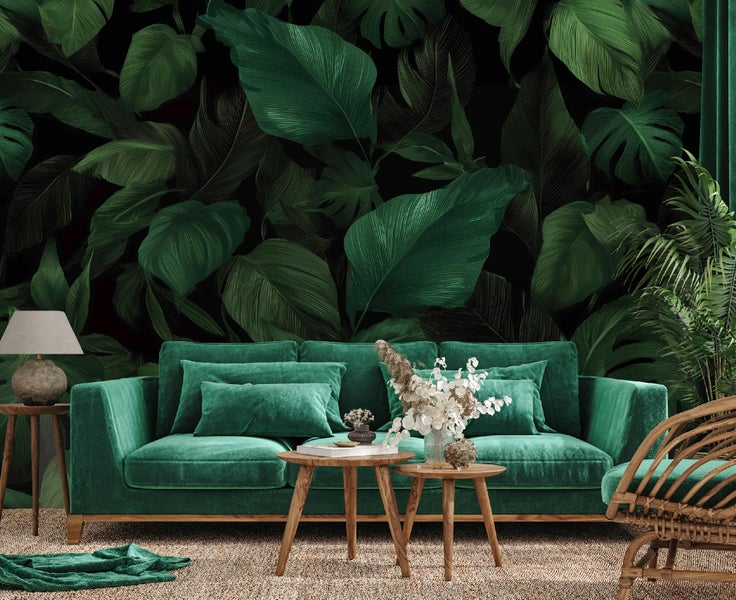 Wohnzimmer mit grüner Couch, Holztischen, Lampe, Dekoration und Tapete mit Pflanzenmotiven.