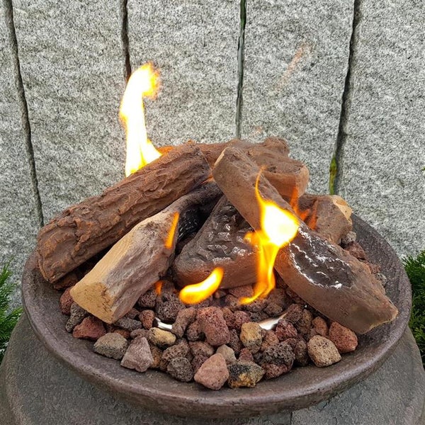 Brennende Keramik-Holzscheite in einer Feuerschale mit Lavasteinen vor einer Steinwand.