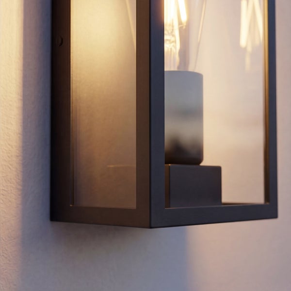 Moderne Außenwandleuchte in Laternenform aus schwarzem Metall und Glas mit sichtbarem Leuchtmittel an einer Fassade.