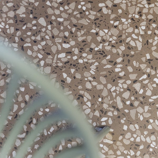 Terrazzo Bodenbelag mit eingearbeiteten Gesteinsstücken in einem Innenraum mit Teilansicht eines Stuhlbeins.