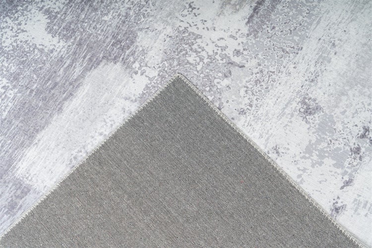 Teppich mit grau-weißem abstraktem Muster und umgeschlagener Ecke zur Ansicht der Rückseite und Kante.