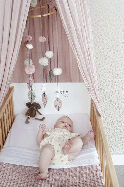 Baby liegt in einem Kinderbett mit Mobile und Stofftier