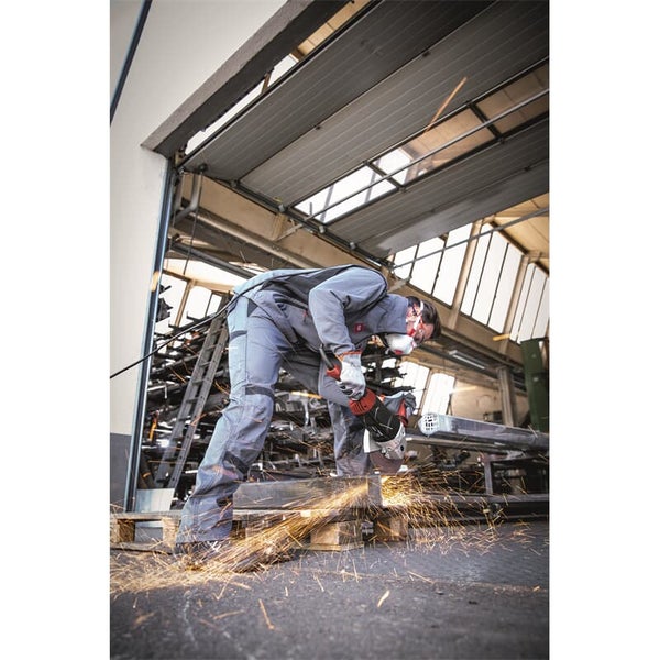 Handwerker mit Schutzkleidung nutzt Winkelschleifer beim Metallzuschnitt in einer Werkstatt mit sprühenden Funken.