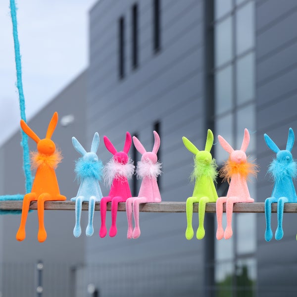 Dekorative Osterhasen aus Plüsch sitzen auf einem Holzbrett.