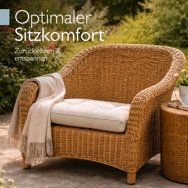 Gartenstuhl aus Korbgeflecht mit hellem Sitzpolster und Decke auf einer Terrasse im Freien.