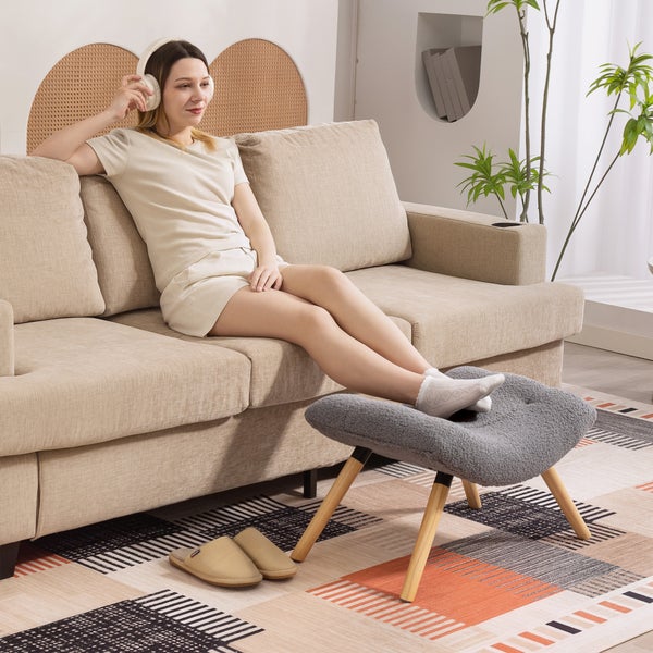 Frau mit Kopfhörern auf Sofa mit Fußhocker und Teppich