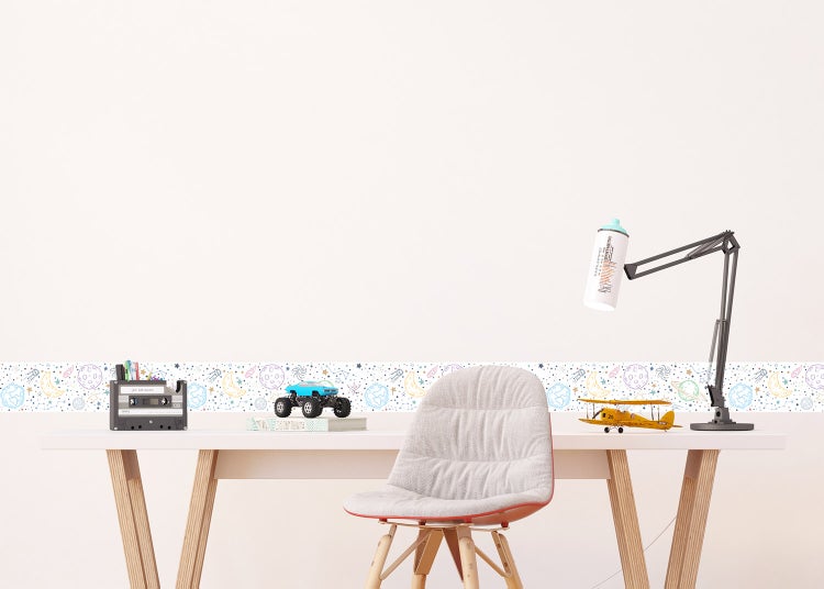 Wandbordüre mit Weltraum-Motiven wie Planeten und Sternen in einem hellen Kinderzimmer über einem Schreibtisch.