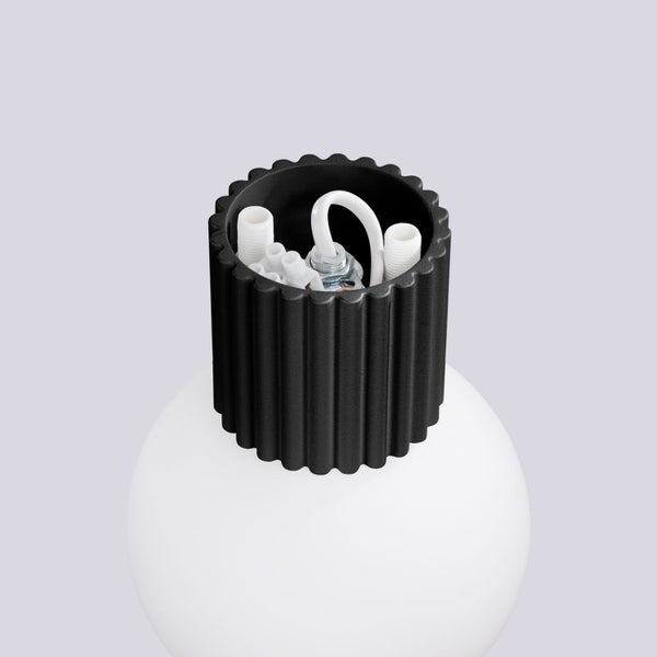 Detailansicht einer schwarzen geriffelten Lampenfassung auf einer weißen Kugelleuchte mit sichtbaren Anschlüssen im Inneren.