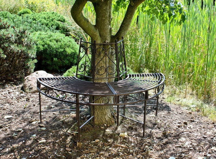 Baumbank aus Metall in einem Garten, halbkreisförmig um einen Baumstamm platziert, mit verzierten Rückenlehnen.