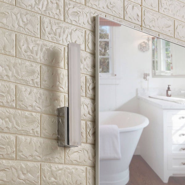 Vertikale Badezimmer-Wandleuchte aus Chrom mit weißem Lichtbalken an einer strukturierten Wand neben einem Spiegel in einem hellen Badezimmer.