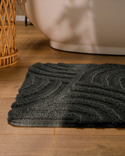 Grüne Badematte mit Wellenstruktur auf Holzfußboden neben einer Badewanne.