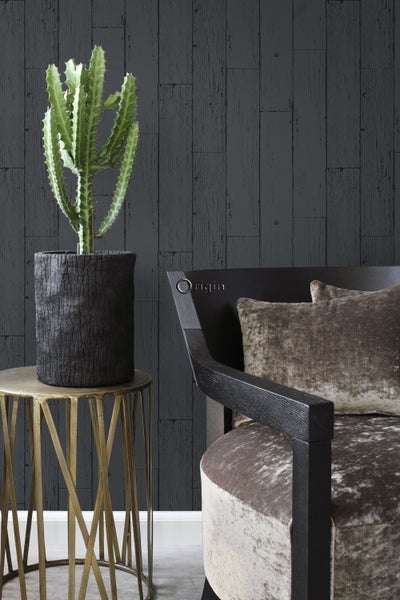 Dekoratives Arrangement mit Kaktus in einem Topf auf einem Beistelltisch neben einem Sessel vor einer Holzpaneelwand
