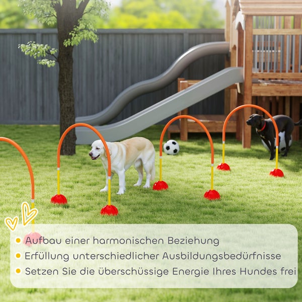 Zwei Hunde trainieren auf einem Agility-Parcours mit Bögen in einem Garten mit Holzspielhaus und Rutsche.