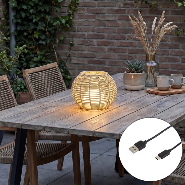 Dekorative Outdoor Tischleuchte in Kugelform aus geflochtenem Material inklusive USB Ladekabel auf einem Holztisch im Garten.