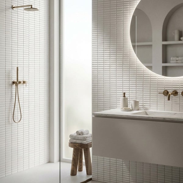 Modernes Badezimmer mit Dusche und Waschtisch mit strukturierten Fliesen, runden Spiegel und Armaturen in Metalloptik.