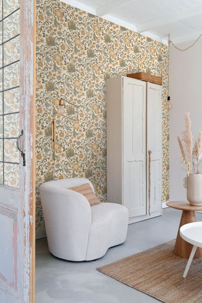 Heller Wohnraum mit floral gemusterter Tapete, Sessel, Schrank aus Holz und Juteteppich.