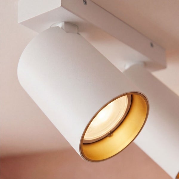 Zylindrischer Deckenstrahler mit goldfarbenem Innenring an weißer Deckenhalterung.