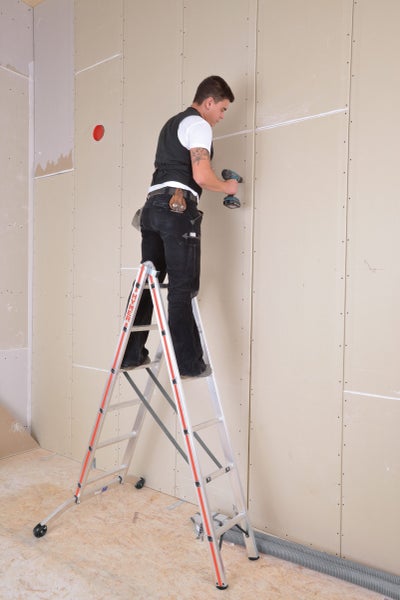 Handwerker auf einer Leiter bei der Montage von Gipskartonplatten mit einem Akkuschrauber.
