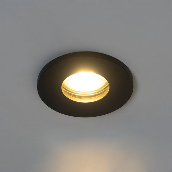 Runder, schwarzer LED-Einbaustrahler in einer Decke mit eingeschaltetem warmweißem Licht.