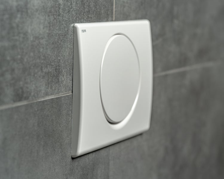 MEPA Betätigungsplatte für Toilettenspülung mit runder Taste, montiert an einer Wand mit grauen Fliesen.