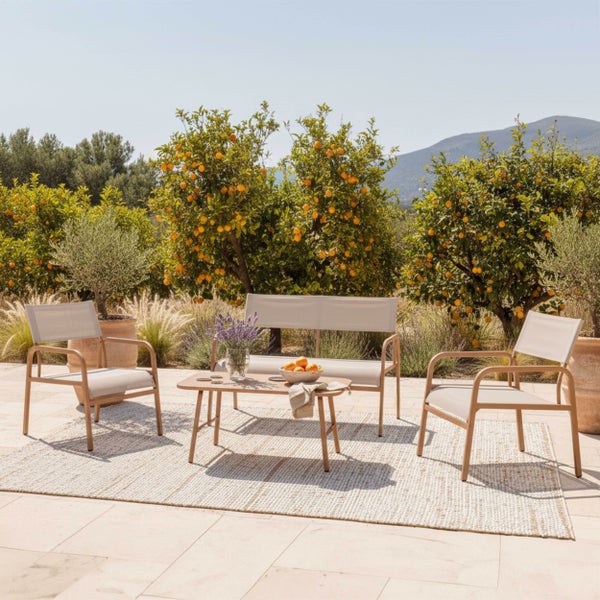 Gartenmöbel-Set bestehend aus einer Bank, zwei Sesseln und einem Loungetisch auf einer Terrasse mit Außenteppich und Pflanzen im Hintergrund.