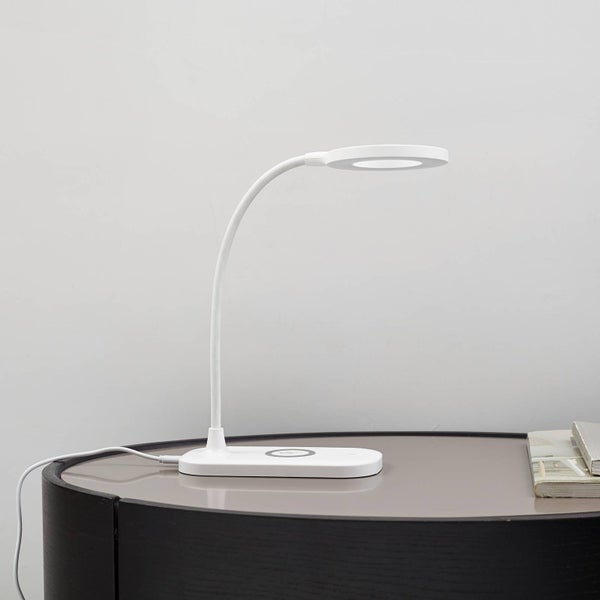 Weiße LED-Schreibtischleuchte mit flexiblem Hals, ringförmigem Leuchtkopf und kabelloser Ladefunktion auf einem Tisch.