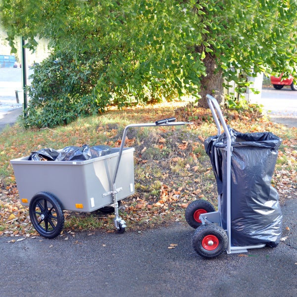 Garten-Transportwagen mit Kunststoffwanne und fahrbarer Müllsackständer mit schwarzem Abfallsack auf einem mit Laub bedeckten Weg im Freien.