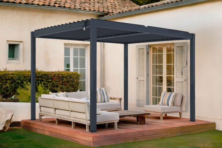 Moderne Pergola mit Lamellendach auf einer Holzterrasse mit Lounge-Möbeln vor einem Haus.
