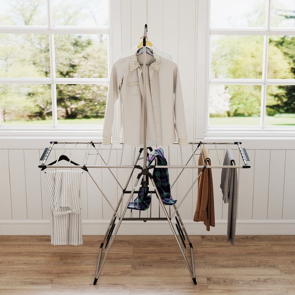 Klappbarer Wäscheständer aus Metall mit Kleidung in einem hellen Raum vor einem Fenster.
