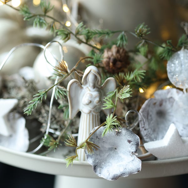Weihnachtliche Tischdekoration mit einer Engel Figur, Tannenreisig, Zapfen und Sternen auf einer Etagere.