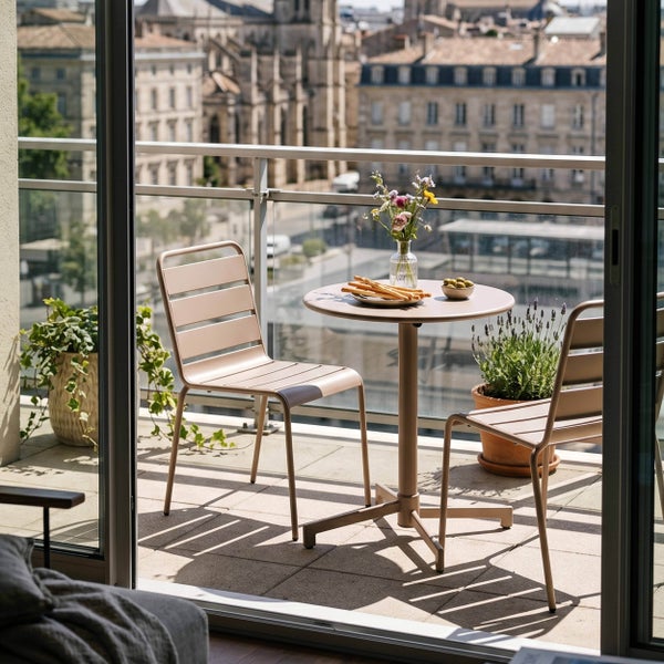 Modernes Balkonmöbel-Set aus Metall mit rundem Bistrotisch und zwei Stühlen auf einer hellen, organisierten Terrasse mit Pflanzen.