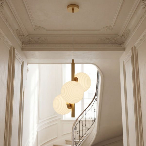 Dreiflammige Pendelleuchte mit geriffelten Glaskugeln und messingfarbenem Metallstab in einem hellen Flur mit Stuckdecke und Treppe.