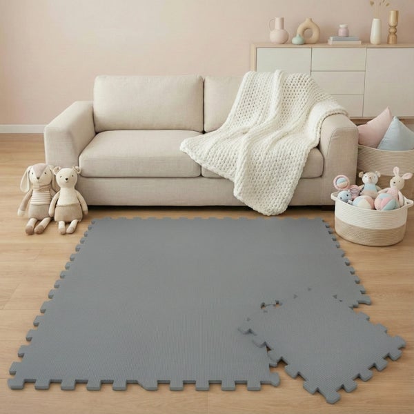 Graue Schaumstoff-Puzzlematte für Kinder auf Holzboden in einem hellen Wohnzimmer mit Sofa und Spielzeug.