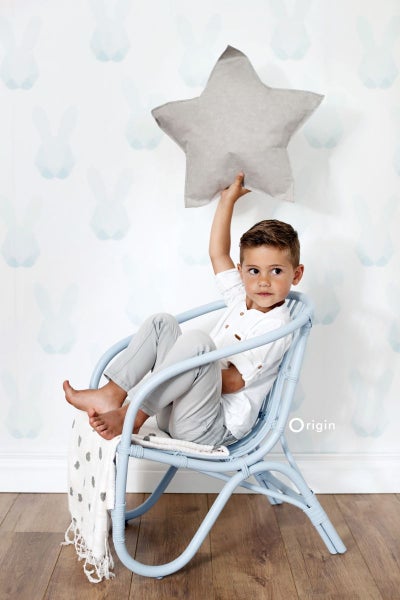 Junge sitzt in einem blauen Rattansessel und hält ein graues Sternkissen.