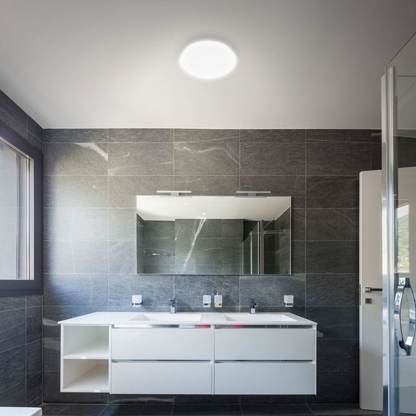 Moderne Badezimmerszene mit runder LED-Deckenleuchte, Doppelwaschtisch in Weiß und dunkelgrauen Fliesen in Natursteinoptik.
