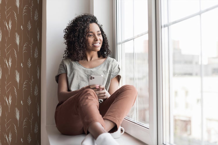 Frau sitzt am Fenster mit Pflanzenmuster-Tapete