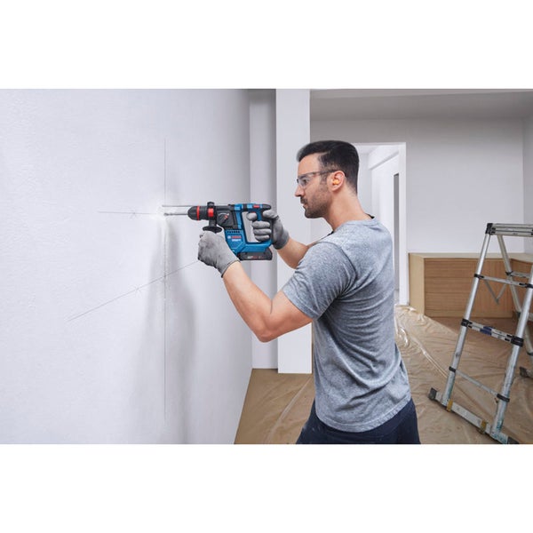 Ein Handwerker bohrt mit einem Bosch Bohrhammer in eine Wand in einem renovierten Innenraum mit einer Leiter im Hintergrund.