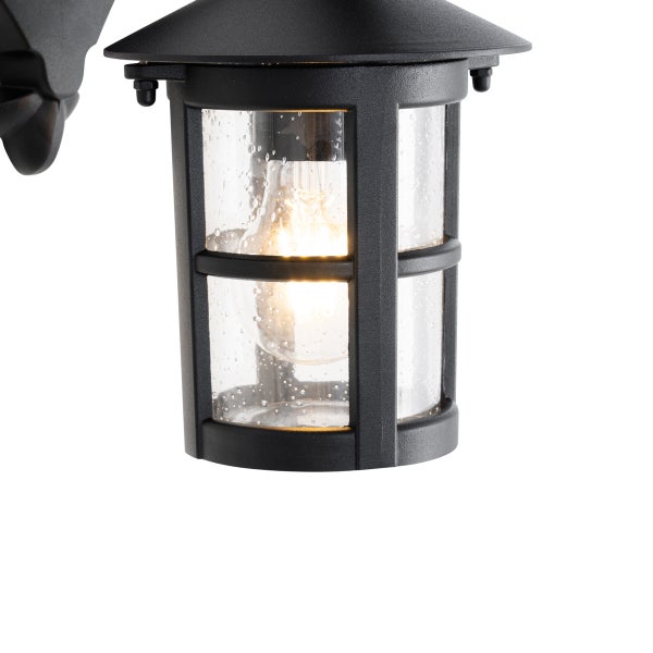 Außenwandleuchte aus schwarzem Metall mit klarem Glas in Tropfenoptik und eingeschaltetem Leuchtmittel.