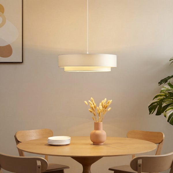 Moderne Pendelleuchte mit zweistufigem Textilschirm über einem runden Holztisch in einem hellen Esszimmer.