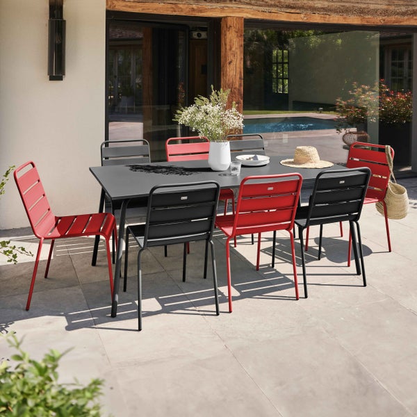 Rechteckiger Gartentisch mit sechs stapelbaren Gartenstühlen aus Metall in Rot und Schwarz auf einer gepflasterten Terrasse.
